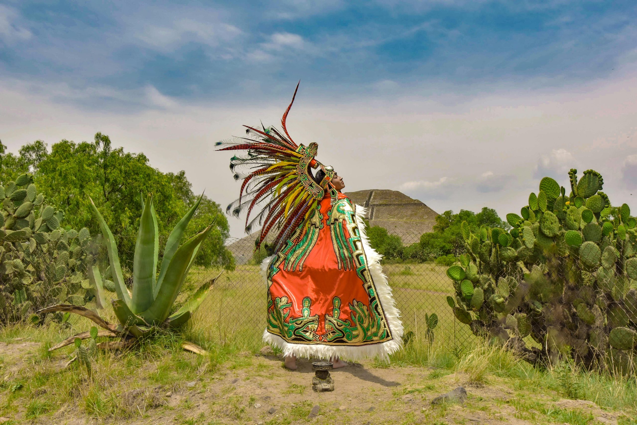 A person in vibrant Aztec attire performing in the natural setting of Teotihuacán, Mexico.