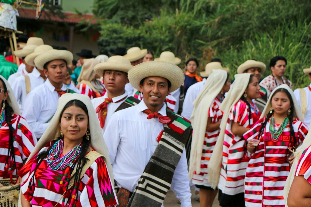 Men and women in traditional Mexican attire partaking in a vibrant outdoor festival parade.